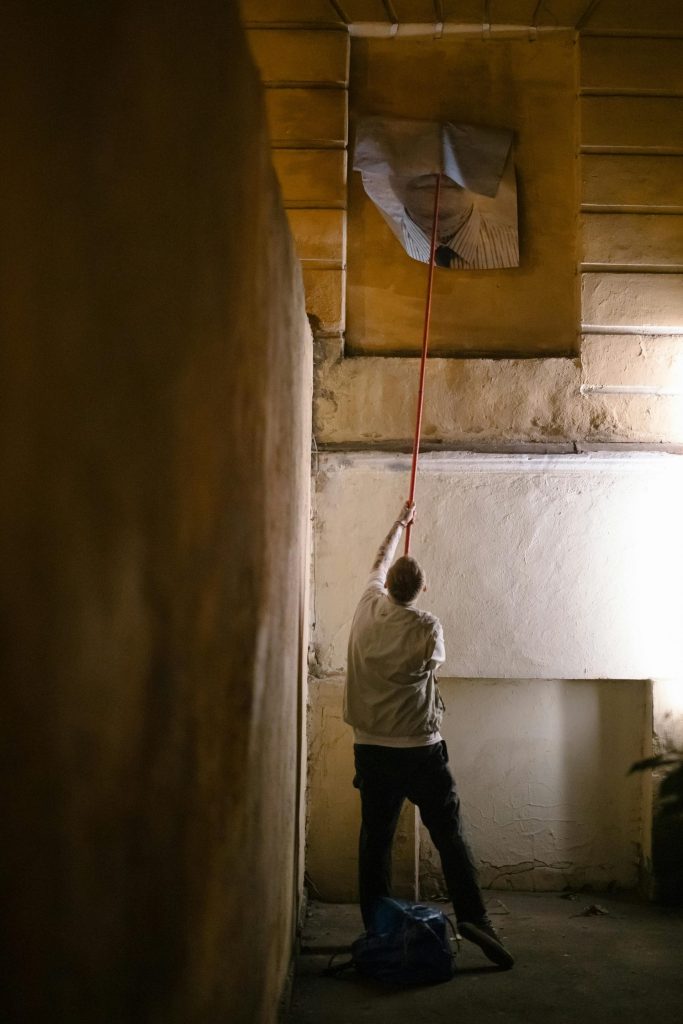 A worker cleaning a city alley with a tool, wearing a white coat, at night.